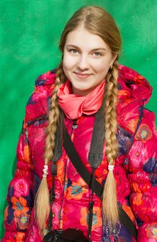 Teen girl with pigtails in red jacket in front of green background.
