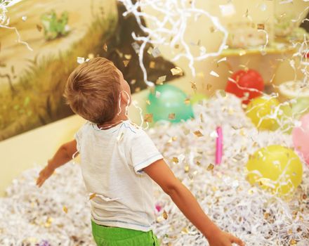 Little boy jumping and having fun celebrating birthday. Portrait of a child throws up multi-colored tinsel and paper confetti. Kids party. Happy excited laughing kid under sparkling confetti shower