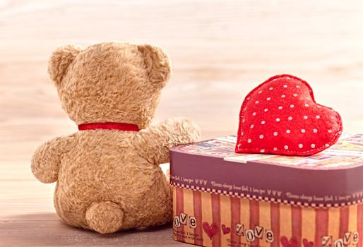 Valentines Day. Teddy Bear Loving sitting alone waiting for love. Heart handmade and gift box, vintage. Retro romantic styled. Sadness concept on wooden background. Back view