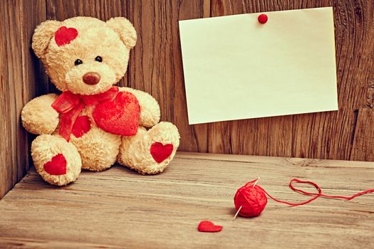 Valentines Day. Teddy Bear Loving with red hearts sitting alone, note and  tangle of sewing thread. Vintage. Retro romantic styled on wooden background. Copyspase