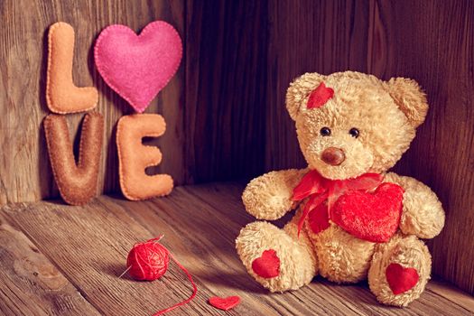 Valentines Day. Teddy Bear Loving cute with red hearts sitting alone, Handmade word Love, tangle of sewing thread. Vintage. Retro romantic styled on wooden background. Copyspase
