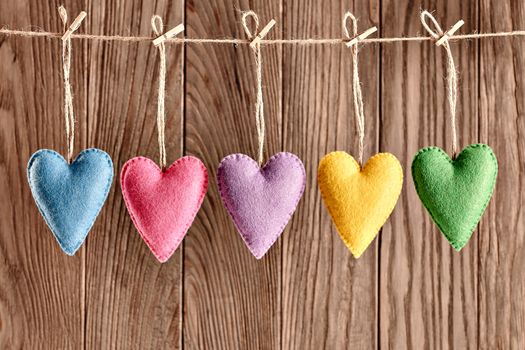 Love hearts, Valentines Day. Hearts set, handmade, hanging on rope. Vintage romantic style on wooden background. Vivid unusual greeting card, multicolored felt, toned, copyspace
