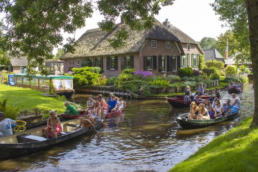 GIETHOORN, NETHERLANDS - AUGUST 05, 2015: Unknown visitors in the sightseeing boating trip in a canal in Giethoorn. The beautiful houses and gardening city is know as "Venice of the North". 