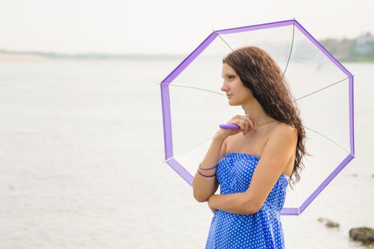 Happy young girl standing with an umbrella on a background of a morning river