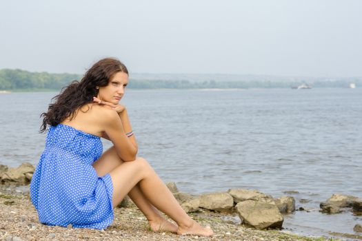 Lonely sad young girl sitting on the river bank