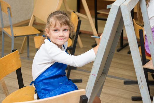 Girl draws pencil on an easel to draw a lesson and looked into the frame