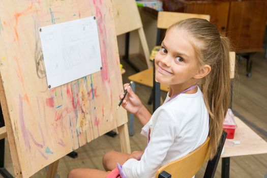 Girl happily looks into the frame on a drawing lesson