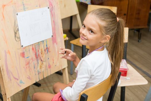 Girl happily looks at the teacher at a drawing lesson
