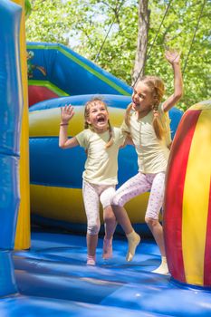 Two girls grimacing happily jumping on an inflatable trampoline