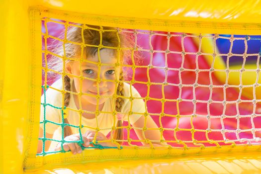 A five-year girl is looking through a mesh trampoline inflatable