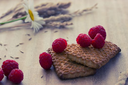 cookies with raspberries and ears on wooden table, toned