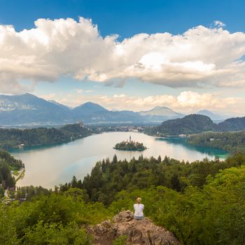 Relaxed female traveler enjoying beautiful panoramic view of Julian Alps, Lake Bled with St. Marys Church of the Assumption on the small island, Bled, Slovenia, Europe.