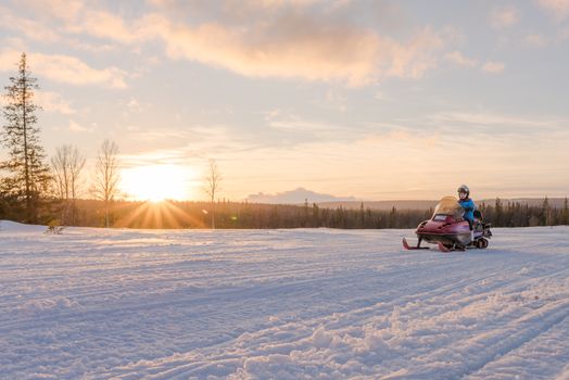 Woman riding snowmobile at sunset. Pure freedom.