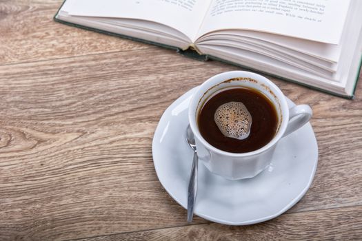 A cup of coffee with a book on a wooden background