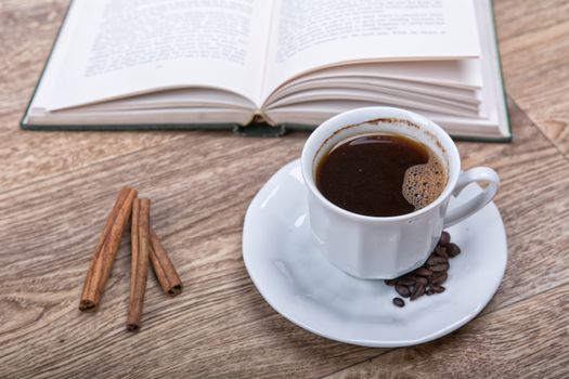 A cup of coffee and cinnamon with a book on a wooden background