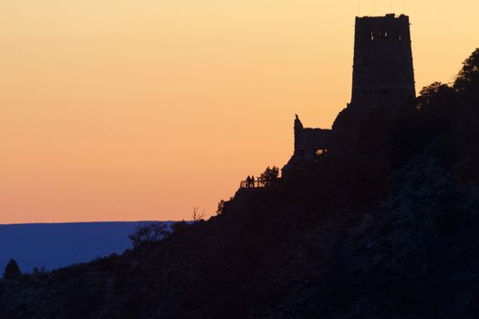 Sunrise colors the sky seen from Grand Cayon's Navajo Point along the South Rim's Desert View Scenic Drive.  Distant silhouette of couple at the Watchtower adds to scene's serenity. 