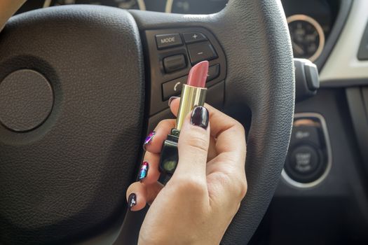 Arm girls with trendy manicure keeps lipstick while driving in the car