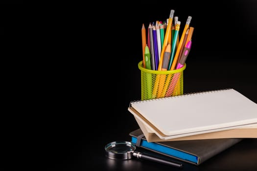 notebook and a container of pencils on black background