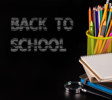 notebook and a container of pencils on black background