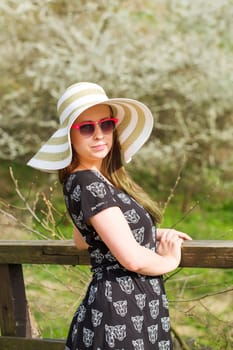 Cheerful fashionable woman in stylish hat, frock and sunglasses Happy brunette girl with long hair in warm spring day