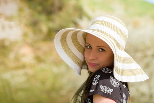 Portrait of cheerful fashionable woman in stylish hat and frock posing outdoor. Happy brunette girl with long hair in warm spring day