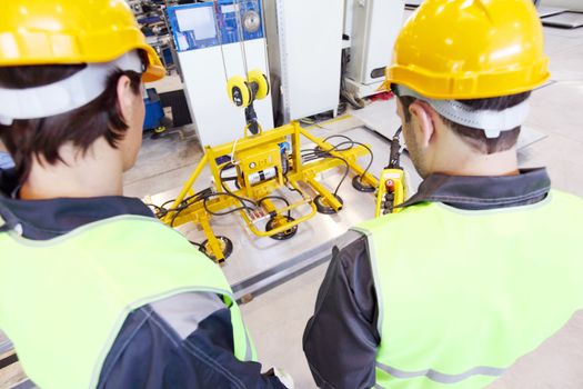 Workers near metal sheet lifting device at factory