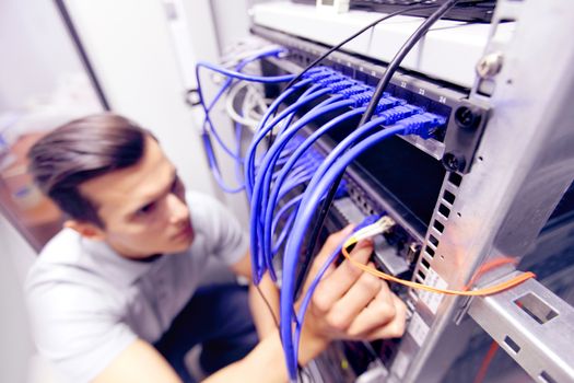 Young engeneer man in network server room connecting wires