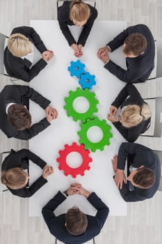 Business team sitting around the table with cogs, teamwork concept