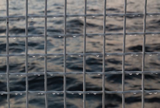 Metallic net with drops against sea background
