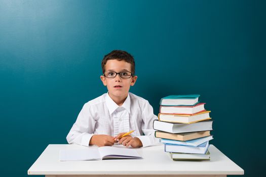 Cute little boy with books on the table, blue background