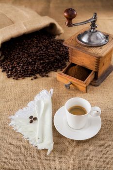 Cup of espresso coffee with coffee-mill and beans on jute