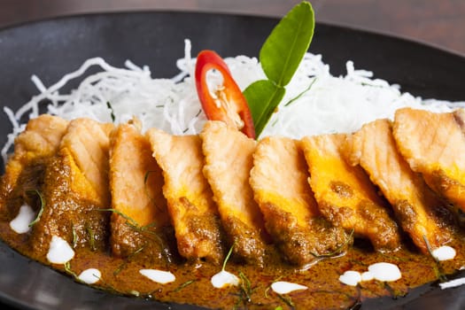 Salmon topped with chili cooking ,On a black plate.