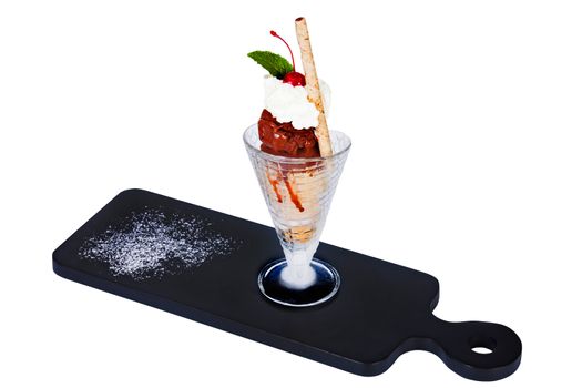 Ice cream with fruit and grated chocolate in a glass on a dark background.