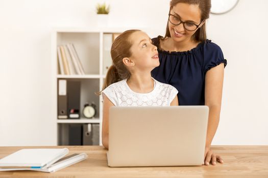 Mother helping her little daughter how to use a computer