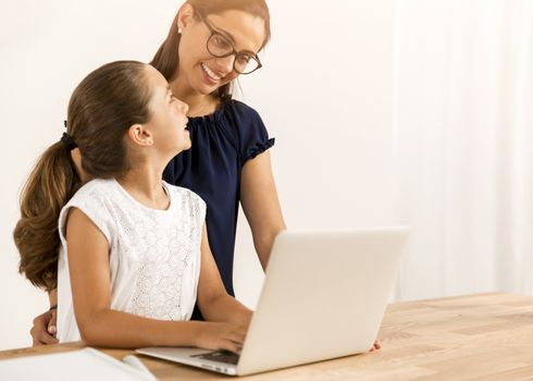 Mother helping her little daughter how to use a computer