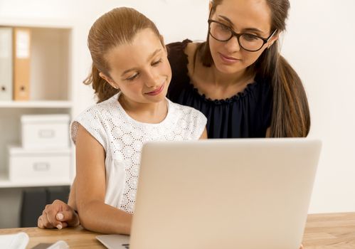 Mother helping her little daughter how to use a computer