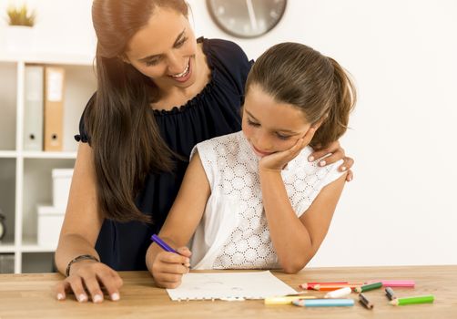 Mother helping her little daughter making drawings