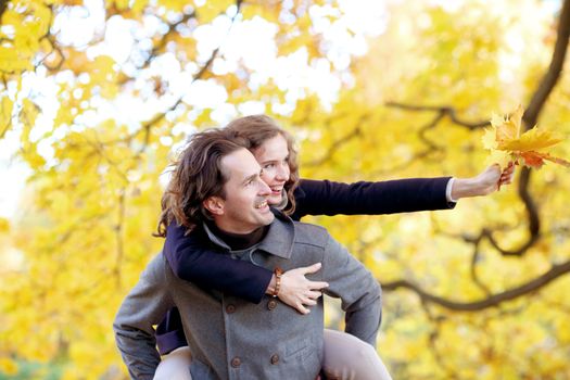 Smiling couple with bunch of leaves hugging over autumn natural background