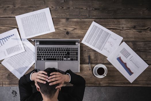 Paperwork and deadline concept - stressed businessman with papers and charts sitting at table in office