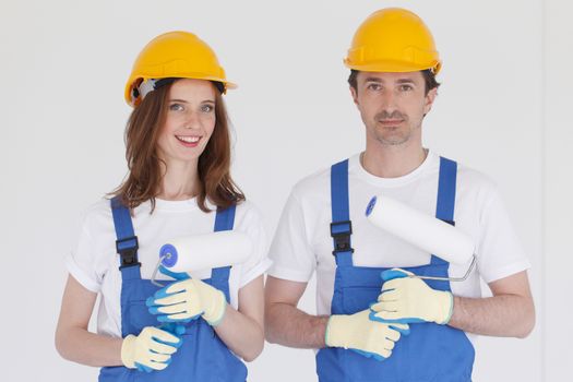 Happy couple in uniform holding paint rollers ready to work