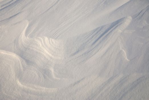 Fine dry powder snow formed into patterns by wind with sunlight and shadows.