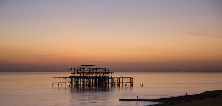 Iconic landmark Brighton West Pier at Sunset, with calm sea and the lights of Bognor Regis in distance.