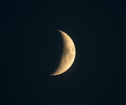 Crescent moon with craters visible in sky not quite black