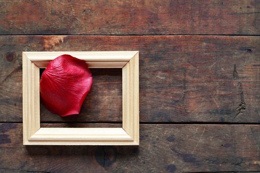 Romance concept. Red rose petal in picture frame on old wooden background