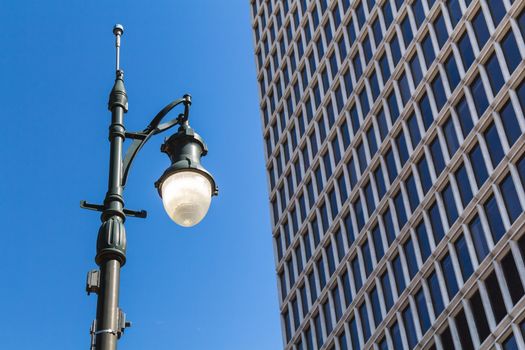 Old design of a street lamp, which is still on in spite of the blue sky day. Detail of a skyscraper. Downtown Detroit, Michigan, USA.