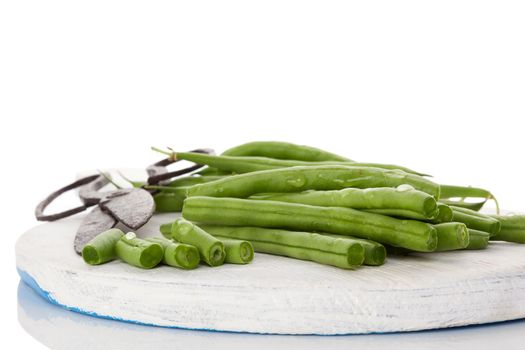 Fresh green beans with water drops on wooden chopping board isolated on white background. Healthy eating. 