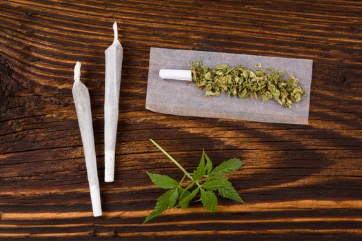 Marijuana background. Cannabis joint, buds and hemp leaves on wooden table. Addictive drug or alternative medicine. 