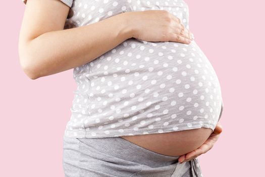 Pregnant beautiful woman touching big belly isolated on pink background. Pregnancy and motherhood. 