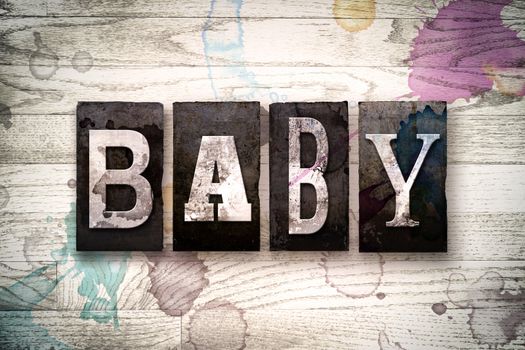 The word "BABY" written in vintage dirty metal letterpress type on a whitewashed wooden background with ink and paint stains.