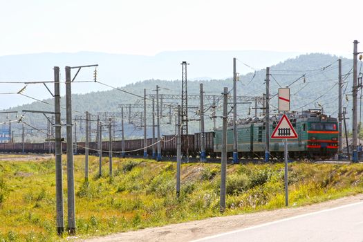 Big green electric locomotive with cars going by rail.